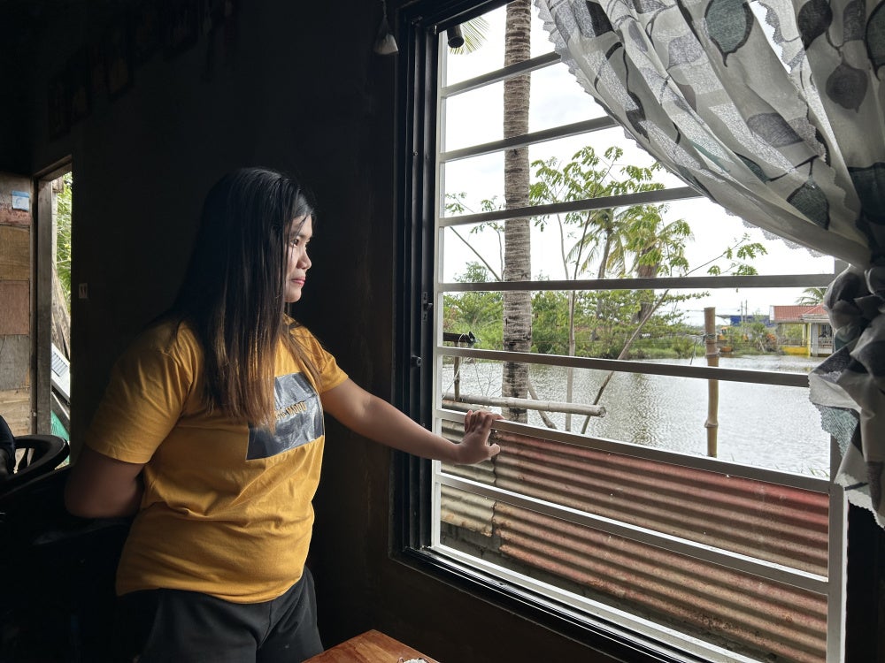 Ria Clarin looks out to water surrounding her house, her daily view since moving to the Pulo relocation site, July 13, 2026.