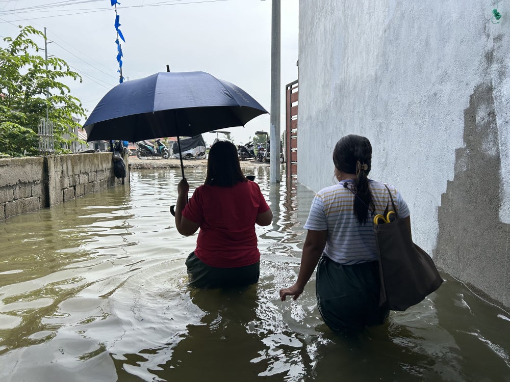 Evangeline Bansil and Rina Tolentino wade through thigh-deep flood waters, July 14, 2026.