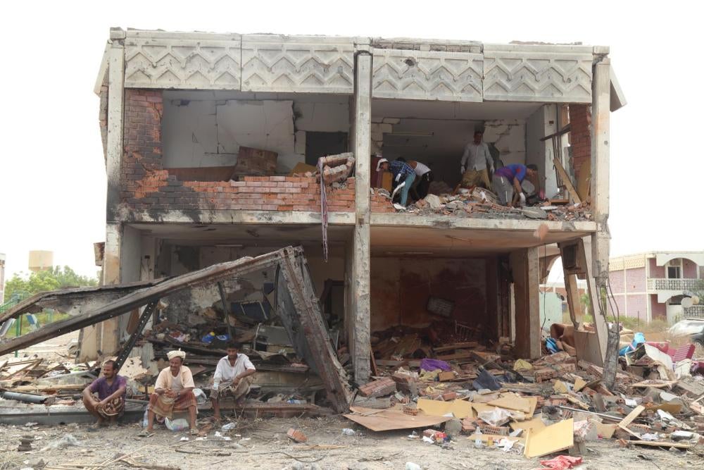 Des hommes assis devant les décombres d’un immeuble résidentiel suite à une frappe aérienne menée le 24 juillet 2015 par la coalition dirigée par l’Arabie saoudite à Mokha, dans le sud-ouest du Yémen.