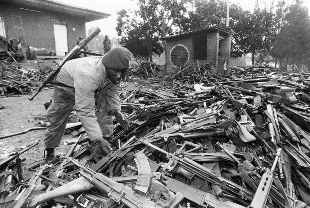 Un soldat zaïrois avec un tas d’armes laissées par des soldats et miliciens rwandais qui avaient fui du Rwanda vers la RD Congo (alors le Zaïre), pour échapper à l’avancée du FPR.