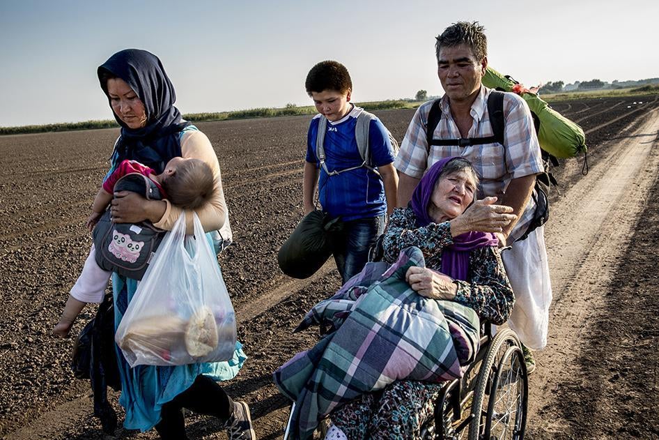 A family from Afghanistan pushes their elderly mother in a wheelchair near Roszke, Hungary after crossing the border with Serbia.  September 13, 2015.