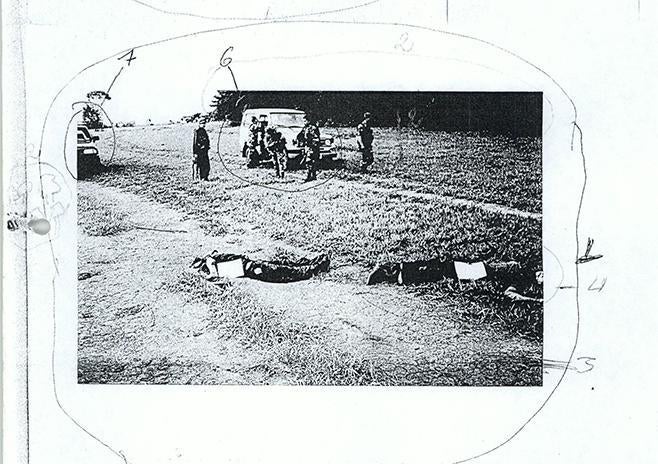 Fotocopia de fotografía de los cuerpos de dos víctimas de presuntas ejecuciones de falsos positivos cometidas en el departamento de Meta en 2004, donde se ven soldados en segundo plano.