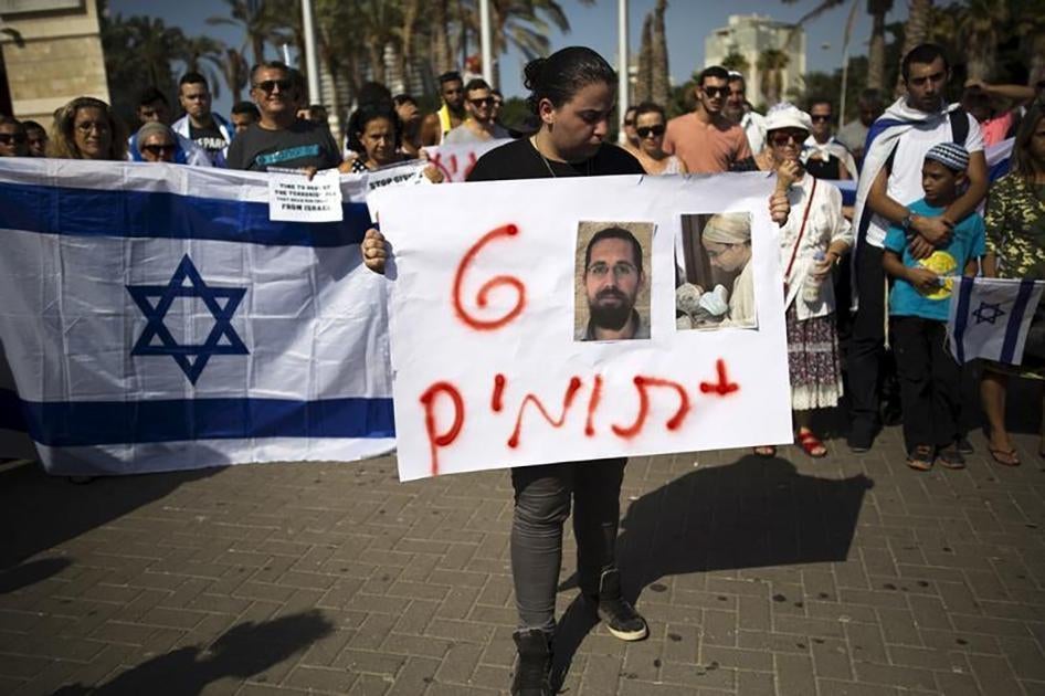 Une femme tient une pancarte sur laquelle figurent des photos d’Eitam et Naama Henkin, tués en Cisjordanie le 1er octobre 2015, et les mots en hébreu « 6 orphelins», lors d'une manifestation tenue trois jours plus tard à Ashdod, en Israël.