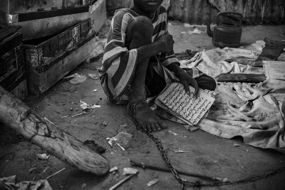 Un jeune talibé, une cheville enchaînée, étudie le Coran dans un daara de la ville de Touba, au Sénégal, en mai 2015.