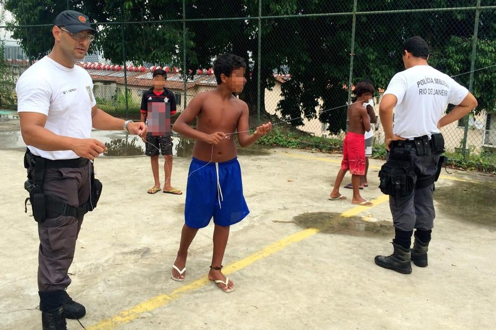 Os policiais militares Thiago Castro (esq.) e Wallace Justo (dir.) brincam com crianças na favela da Mangueira em 14 de Janeiro de 2016. 