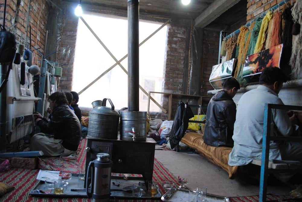 Children weave carpets at looms in West Kabul. Weavers sit in one position for hours and perform repetitive motions using sharp equipment, risking injury.