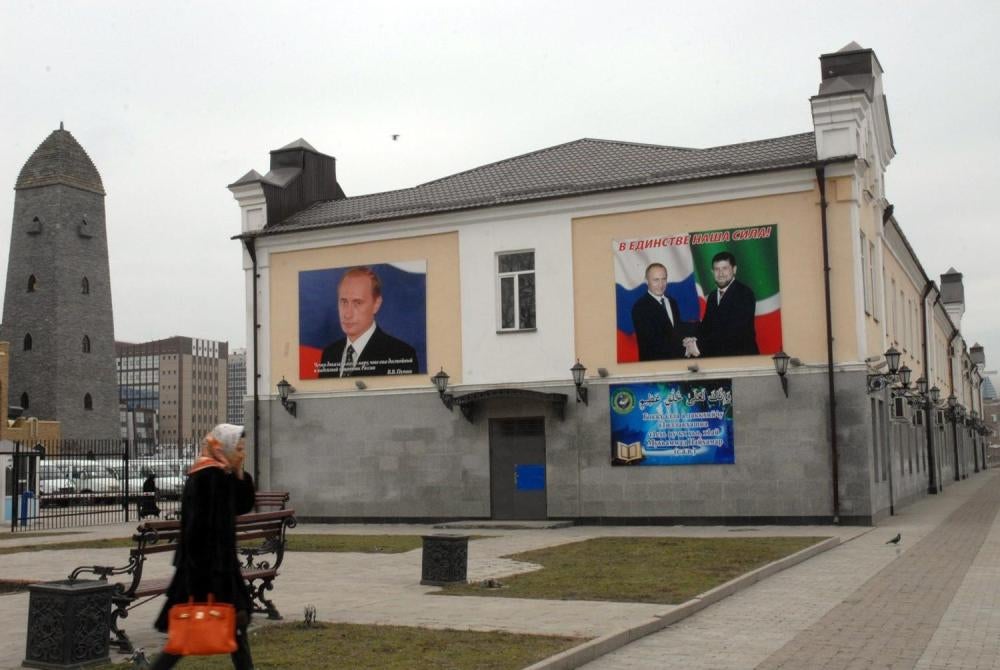 Women walking in the center of Grozny next to a building with portraits of Ramzan Kadyrov and Vladimir Putin. 