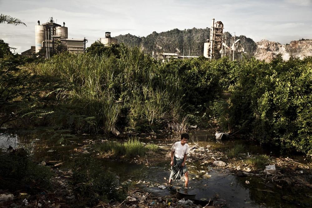 A man walks through a polluted river that flows through a village overshadowed by a cement factory owned by the Burmese military-controlled Myanmar Economic Corporation in the Hpa-an region of Karen State.