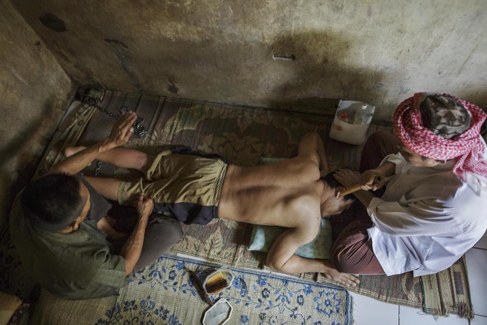 Haji Hamden, an Islamic faith healer, chants as his assistant Abdul slaps the leg of a shelter resident at Pengobatan Alternatif Nurul Azha, a traditional healing center, in West Java.