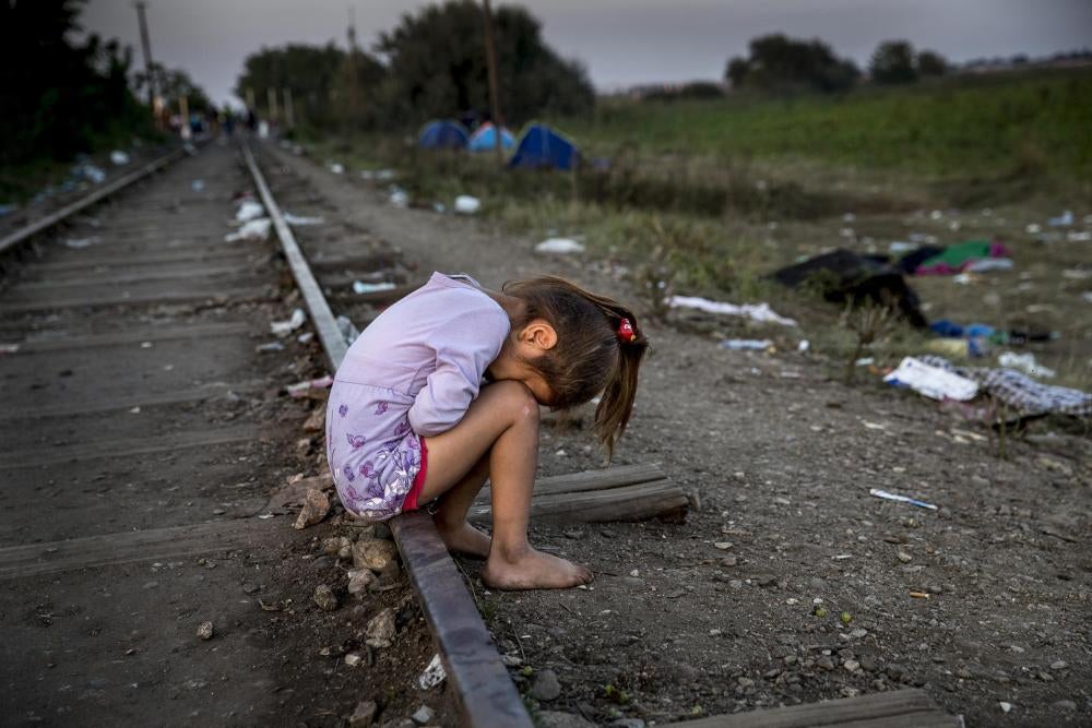Une enfant exténuée pleure sur les voies de chemin de fer entre la Serbie et la Hongrie à la nuit tombée et sa famille discute à proximité pour savoir s’ils doivent traverser le pays vers la Hongrie et s’exposer à une détention temporaire. 