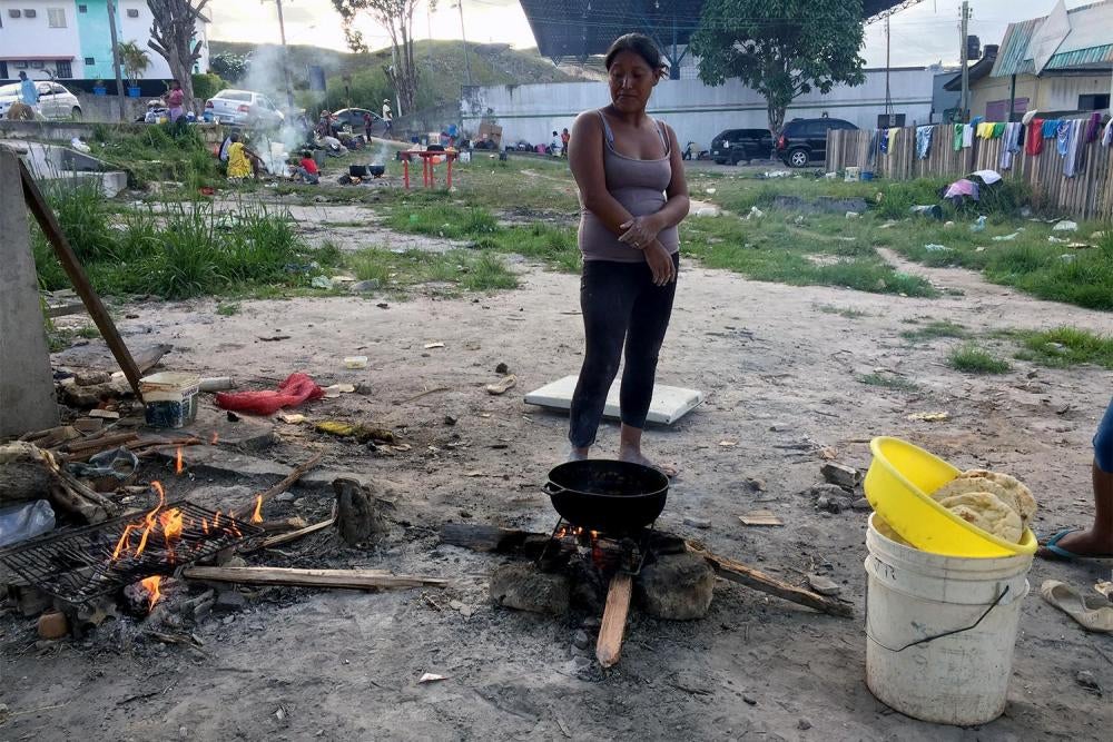 A Venezuelan Warao indigenous woman cooks at a vacant lot by the bus station in Pacaraima, Brazil, where she is staying with about 100 other members of her community.