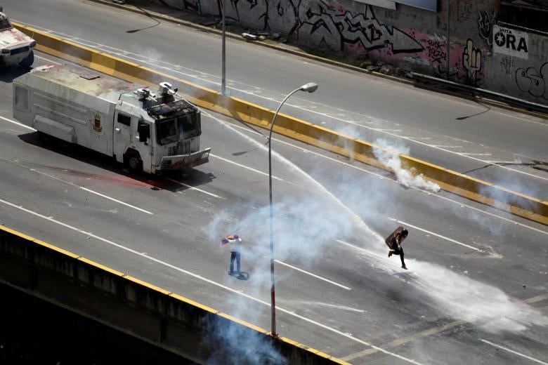 An opposition supporter is hit by a water canon while clashing with riot police in Caracas, Venezuela. May 18, 2017. 