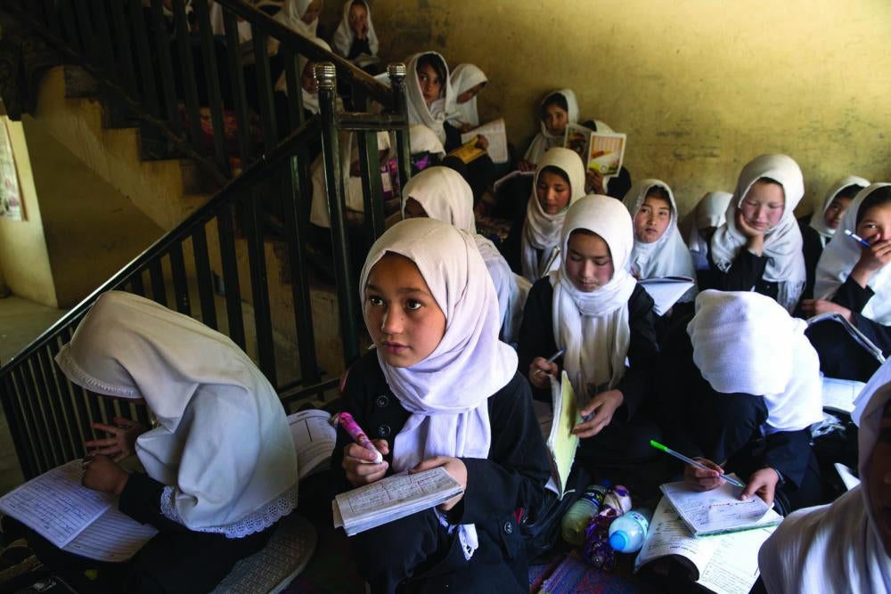 Girls sit for lessons on a stairwell inside a school building.
