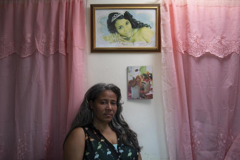 Rosa Hernández stands in her home below a photo of her daughter, Rosaura Almonte Hernández, who died in 2012 at age 16.