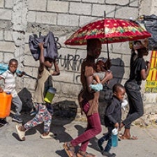 Children and adults carry belongings on street. 