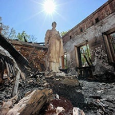 A figure stands within walls of destroyed home. 