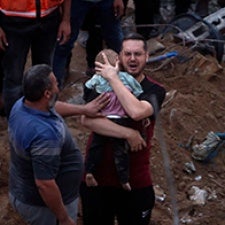 Individuals hold child amidst rubble. 