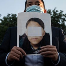 Person holds up poster displaying obscured face of a child. 