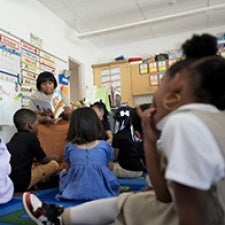 Children face teacher in classroom. 