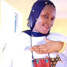 Figure holds hand to chest and faces camera. 