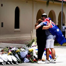Two figures hug in front of vigil. 