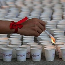 Hand wrapped in red ribbon holds candle over paper cups. 
