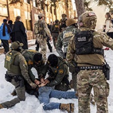 People in military garb detain individual on the floor. 