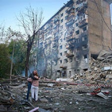 Two figures stand amidst rubble in Ukraine. 
