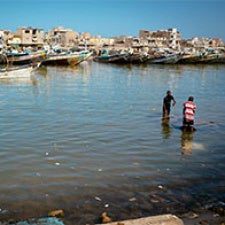 Two figures stand in body of water. 