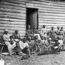 Black and white image of large group sitting outside home. 