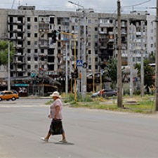 Single figure walks on street near rubble. 