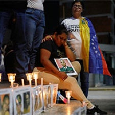 Figures place candles and images near memorial site. 