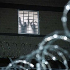 People seen through the window of a detention facility surrounded by barbed wire