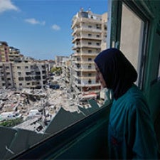 Woman standing in window looking out over rubble in Tyre, Lebanon 