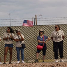 Four figures stand in front of wall and American flag. 