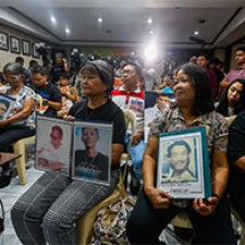 Rows of people sitting, holding photos of their loved ones in their laps
