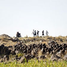 Field with figures standing on hill. 