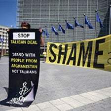 Protester holds sign in front of yellow "shame" banner. 