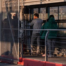 A group stands facing away from camera in detention center.