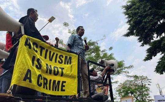 Individuals hold up yellow banner reading, 'Activism is Not a Crime'. 