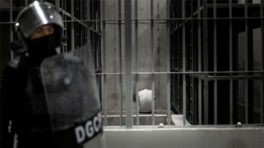 Police figure stands in front of cells. 