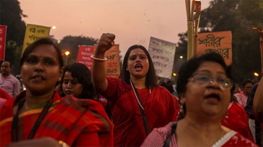 Figures wear red and hold protest signs. 