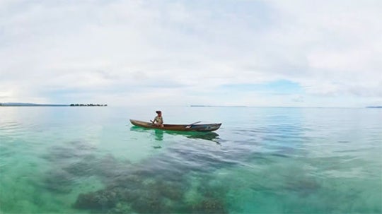 Two figures sit on a small boat in open water. 