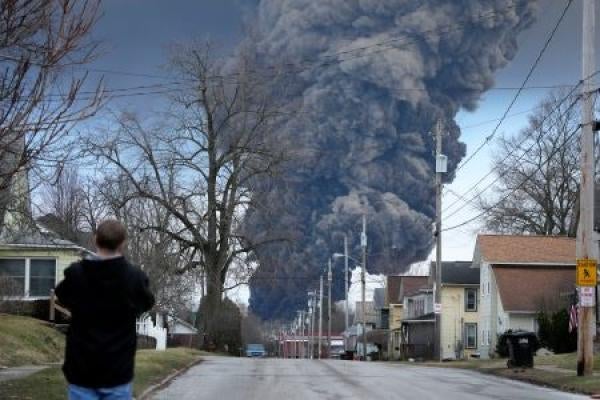 A man takes photos as a black plume rises over East Palestine, Ohio, as a result of a controlled detonation of a portion of the derailed Norfolk Southern trains, February 6, 2023.
