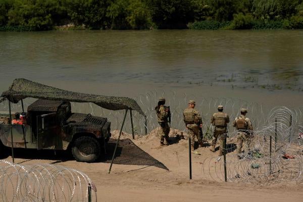 Guardsmen stand by a river lined with razorwire