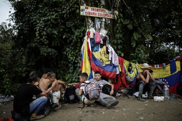 Migrants sit under a sign marking the Panama-Colombia border