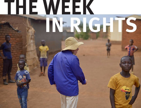 Photo of man in blue shirt and white hat, walking among children in Malawi 