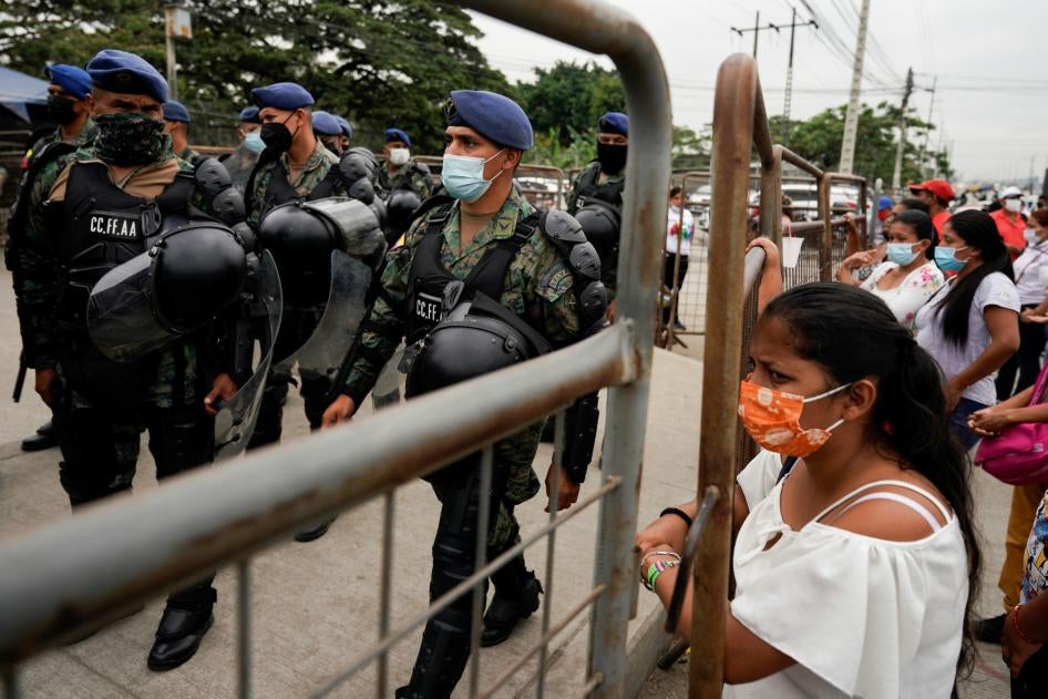 Soldiers walk carrying riot gear, while civilians look in behind barricades