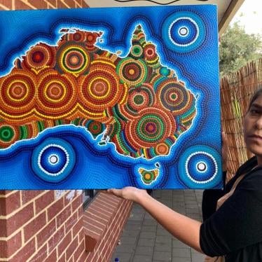A woman holds up a colorful painting that depicts the Australian continent