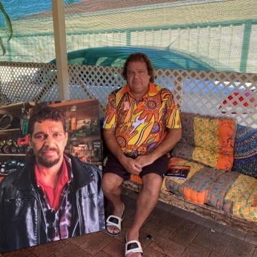 A man sits on a couch next to a large photo of his brother